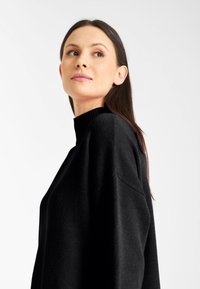 Schwarzer Rollkragenpullover mit lockerer Passform, gestrickter Textur und überschnittenen Schultern. Der glatte Stoff legt sich elegant über den Körper.