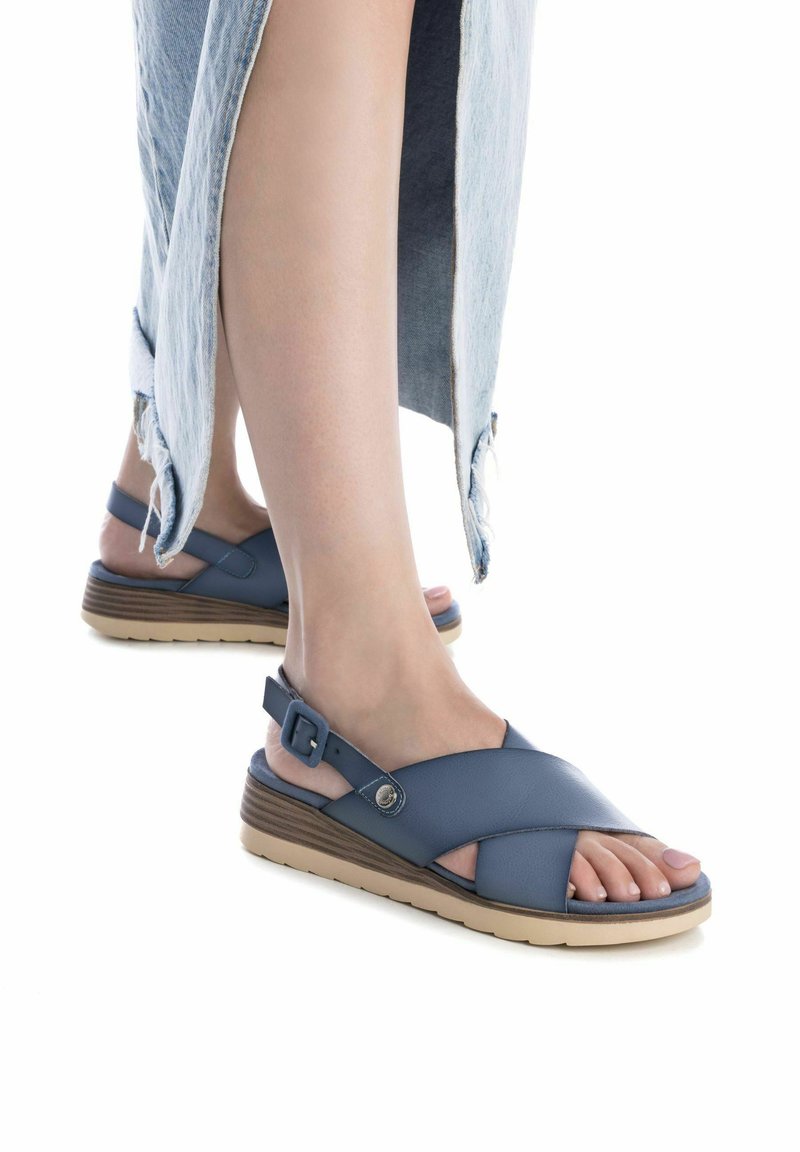 Sandalias de cuero azul con un diseño de tiras cruzadas, que cuentan con un cierre de hebilla y una suela de cuña en marrón claro. Color azul con una textura suave.