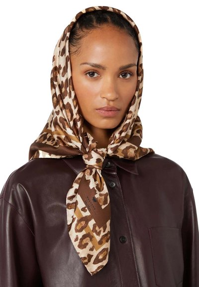 Γυναίκα με απαλό δέρμα που φοράει καφέ δερμάτινο πουκάμισο και ένα δεμένο μπεζ και καφέ φουλάρι με λεοπάρ σχέδιο πάνω από το κεφάλι και τους ώμους της.