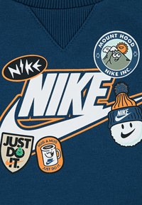 Navy plava dukserica s raznim zakrpama: Nike logo, dizajn planine Hood, "Samo uradi to," logo šolje i smajli u kapici.