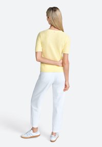 Pull court texturé jaune à manches courtes, pantalon droit blanc et baskets bleu clair avec une semelle blanche. Détail de design simple au dos.