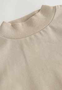 Lys beigefarvet højhalset sweater med en glat tekstur, ribbet krave og et minimalistisk design. Flad visning fremhæver stoffets kvalitet.