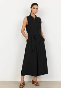 Svart ärmlös jumpsuit med krage, framsidan med dragkedja, två bröstfickor, ett knytbälte i midjan och vida ben.