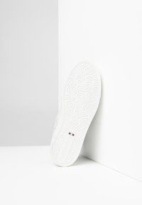 Semelle de sneaker blanche avec un motif en vagues texturé, présentant un détail de drapeau italien rouge, blanc et vert ainsi qu'une marque dans un design en relief subtil.