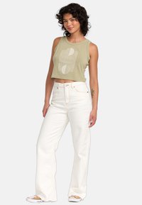 Geperforeerd olijfgroen tanktop met grafisch ontwerp, gecombineerd met hoge witte wijde jeans en witte sneakers met tan details.