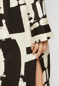 Rochie cu model alb-negru, cu o textură mătăsoasă și un slit pe lateral, având o mânecă largă și o mână vizibilă aproape de tiv.