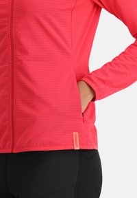 Giacca fucsia con zip, texture a righe, maniche lunghe e tasche; presenta un'etichetta con logo a contrasto sull'orlo.