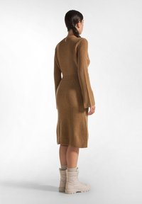 Braunes geripptes Strickkleid mit langen Ärmeln, körpernaher Silhouette und Rundhalsausschnitt, kombiniert mit beigen gepolsterten Stiefeln.