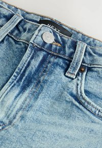 Jeans en denim bleu avec un délavé, dotés d'un bouton en argent et de surpiqûres en cuivre. Comprend des passants de ceinture et des poches avant.