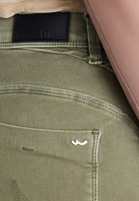 Pantalones verde oliva con una tela texturizada. Presentan una etiqueta de cuero negro con "LTB" y un logo plateado en el bolsillo trasero.