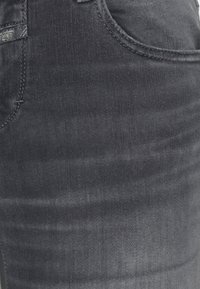 Jeans de mezclilla en un color gris oscuro con una textura suave. Presenta costuras de contraste y un acabado sutilmente desgastado. Incluye una etiqueta en la cinturilla.
