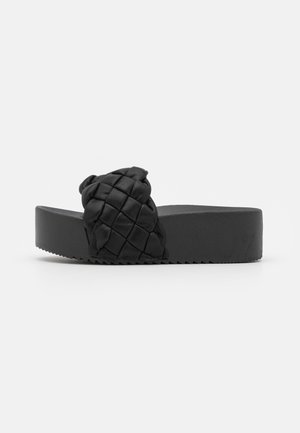 Zwarte platform sandalen hebben een geweven leren bovenkant met een platte zool en een gestructureerd oppervlak, ontworpen voor comfort en casual gebruik.