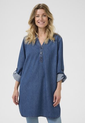Denim-paita, puolipitkä, V-kaula-aukolla, nappikiinnityksellä varustetuilla käärittävillä hihoilla, которые ovat tasaisessa keskisinisen värissä ja pehmeässä tekstuurissa.
