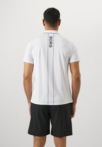 Weißes Poloshirt mit schwarzen Liniendetails und "BORG"-Text auf dem Rücken, kombiniert mit schwarzen Shorts. Glattes, leichtes Gewebe.