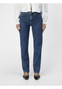 Jeans dritto blu scuro in tessuto denim. Presentano un classico design a cinque tasche e una texture sbiadita. Indossati con scarpe nere a punta.