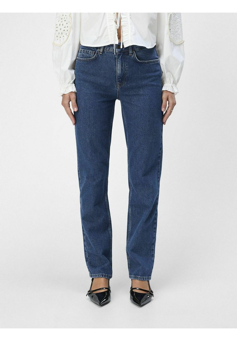 Jeans dritto blu scuro in tessuto denim. Presentano un classico design a cinque tasche e una texture sbiadita. Indossati con scarpe nere a punta.