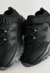 Black athletic shoes made of synthetic materials, featuring textured fabrics, elastic laces, and a rugged sole with deep treads.