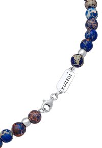 Bracelet en perles avec des pierres marbrées bleues, beiges et rouges, accents en argent et un fermoir en homard avec une étiquette KUZZOI.