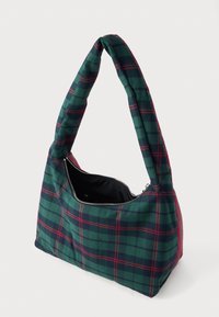 Sac à bandoulière en tissu à carreaux verts et bleu marine, avec une forme courbée, une fermeture zippée et une poignée douce. Doublure intérieure noire visible.