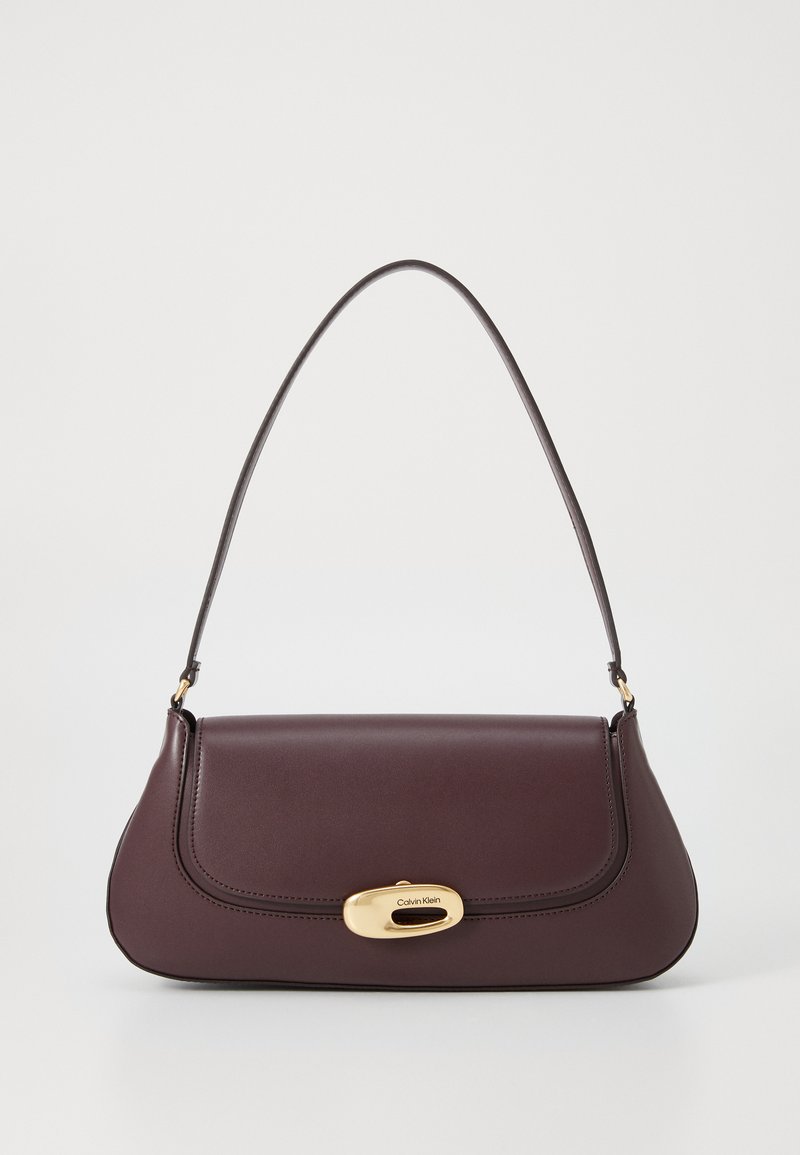 Sac à main en cuir bordeaux avec une forme courbée, une bandoulière réglable et un fermoir en hardware doré affichant le logo Calvin Klein.