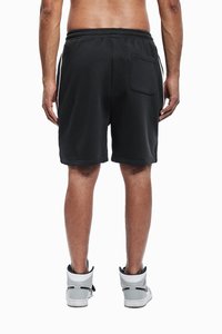 Schwarze Sportshorts mit elastischem Bund und einer Gesäßtasche, kombiniert mit hohen grauen Sneakers. Glattes Material und lockere Passform.