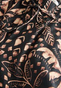 Tissu noir avec des motifs botaniques et géométriques marron et un cordon noir noué en nœud près du bord supérieur.