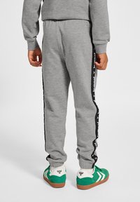 Grå sweatpants med elastisk midja, sidostriper med text och ribbade muddar. Matchade med gröna och vita sneakers.