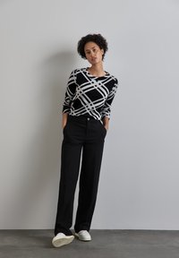 Svart och vit mönstrad tröja med rund halsringning, kombinerad med svarta, vida byxor och vita sneakers på en texturerad yta.