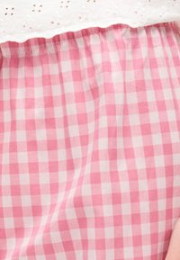 Εγγύς πλάνο ροζ και λευκού καρό υφάσματος με ραφή που μαζεύει κάτω από λευκή δαντέλα με τρυπητό σχέδιο.