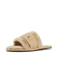 Chausson à glisser en fausse fourrure beige avec une large bande, texture douce, design ouvert au niveau des orteils et semelle plate. Comprend un petit détail de marque métallique.