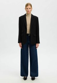 Melns fakturēts žakete, bēšs augstas apkakles džemperis, plata piegriezuma tumša džinsa bikses un melni smailpirkstu apavi. Vienkāršs dizains ar ievērojamu kārtaino izskatu.