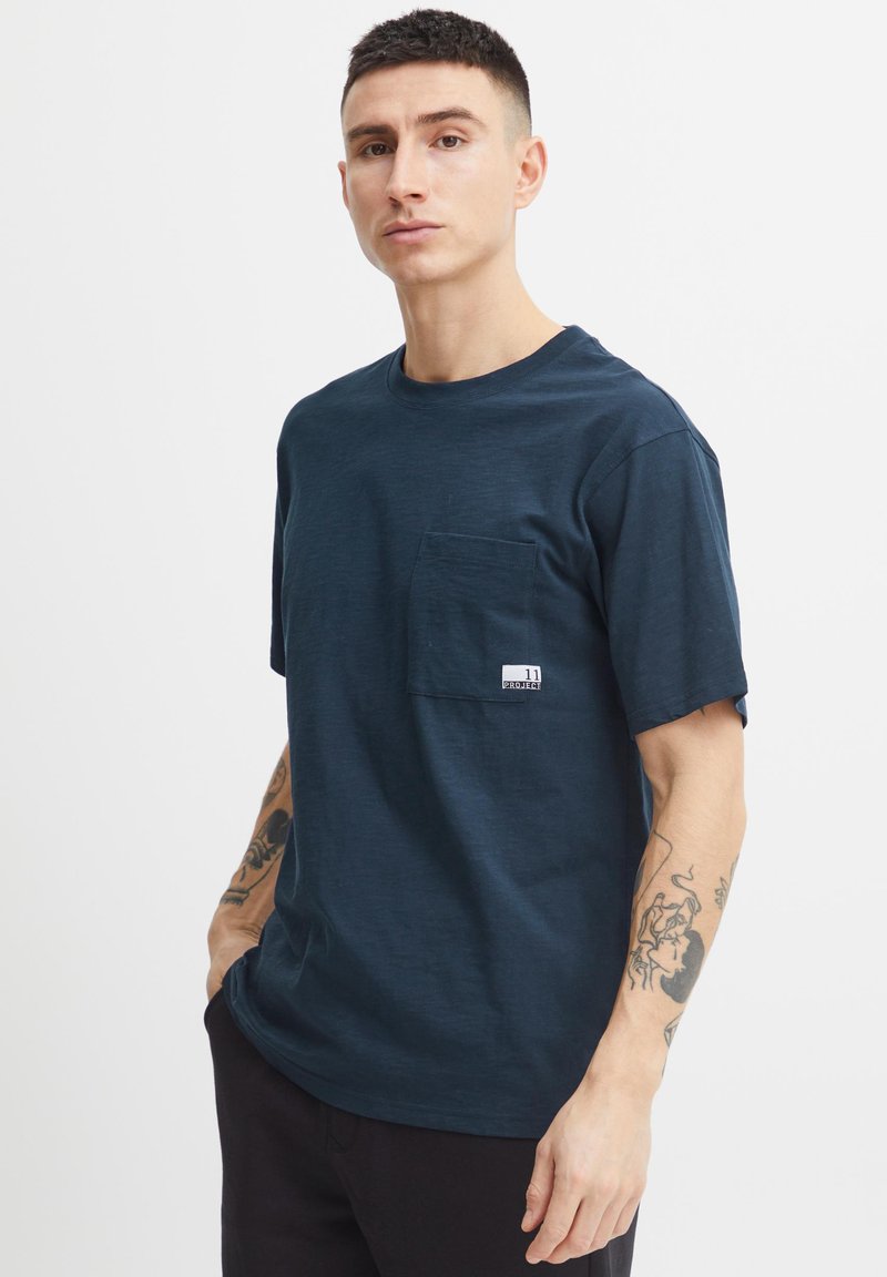 Navy blue short-sleeve t-shirt in a soft, textured fabric featuring a chest pocket and a label near the hem. The fit is relaxed.