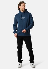 Felpa navy in tessuto dalla superficie liscia, con stampa del logo sul davanti, coulisse e polsini a coste. Abbinate a jeans neri e sneaker bianche.