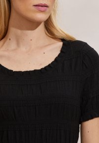 Maglietta nera con texture, colletto a volant e righe orizzontali. Maniche corte e materiale leggero creano una vestibilità comoda.