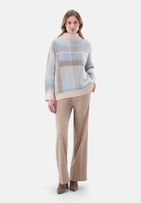 Helle blaue und beige gemusterte Rollkragensweater mit entspannter Passform, kombiniert mit beigen weit geschnittenen Hosen und taupefarbenen Absätzen.