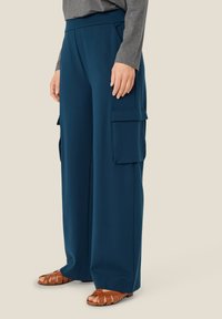 Donkerblauwe wijdvallende cargobroek van een gladde stof, met twee grote zijzakken en een elastische tailleband voor comfort.