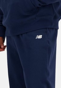 Conjunto de sudadera y pantalones de chándal en azul marino, con una textura suave, puños acanalados y un logo blanco "NB" en la pierna del pantalón.