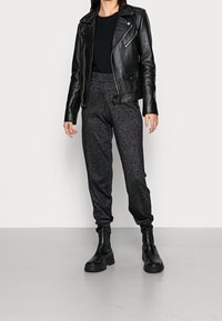 Černá kožená motorkářská bunda se stříbrnými zipy, kombinovaná s přiléhavými černými textured tepláky. Model nosí robustní černé kotníkové boty.