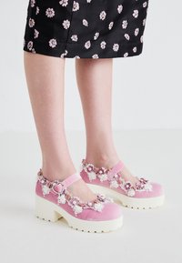 Roze fluwelen Mary Jane-schoenen met witte platformzolen, versierd met bloemapplicaties en kantdetails rondom de opening en de enkelband.