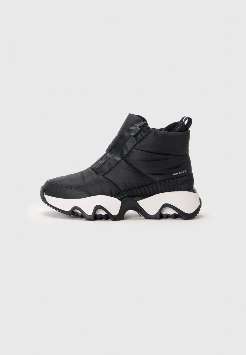 Bottine noire imperméable avec tige matelassée, semelle blanche épaisse avec motif ondulé noir et fermeture éclair latérale sur fond neutre.