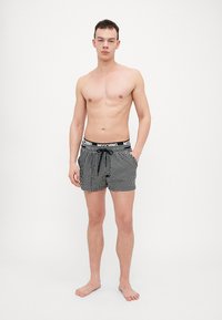 Costum de baie în carouri alb-negru, cu talie elastică care prezintă un logo de marcă, conceput cu o croială lejeră și buzunare laterale.