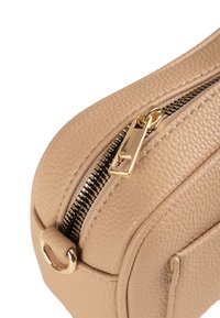 Borsa in pelle beige con finitura testurizzata, dotata di una cerniera e accessori in oro, e un anello decorativo su un lato per dettagli di stile.