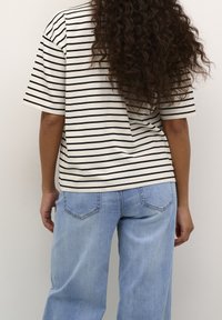 Camiseta de algodón a rayas en crema y negro, corte relajado con mangas cortas, combinada con vaqueros de mezcla ligera de corte holgado, con bolsillos traseros.