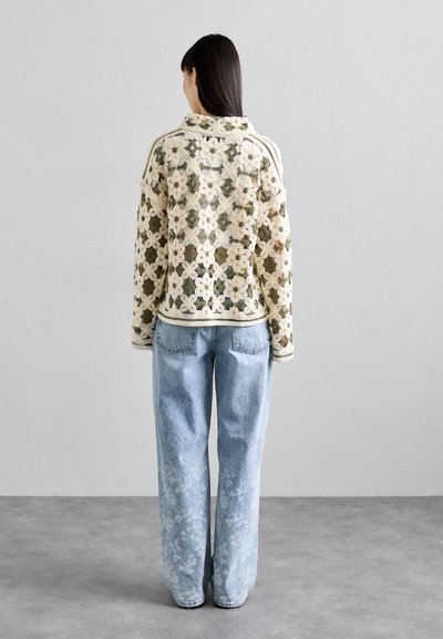 Heklet cardigan i kremfarge og grønn, med blomstermønster, lange ermer og løs passform. Kombinert med lys blå, slitte vide jeans.