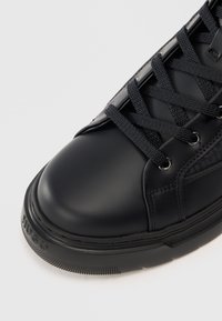 Baskets en cuir noir avec un bout arrondi, des lacets texturés et des œillets en métal. Présente une semelle en caoutchouc épaisse avec une marque sur le côté.