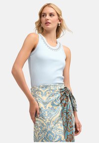 Light blue ribbed tank top with decorative beading at the neckline, paired with a patterned wrap skirt featuring blue and brown florals.