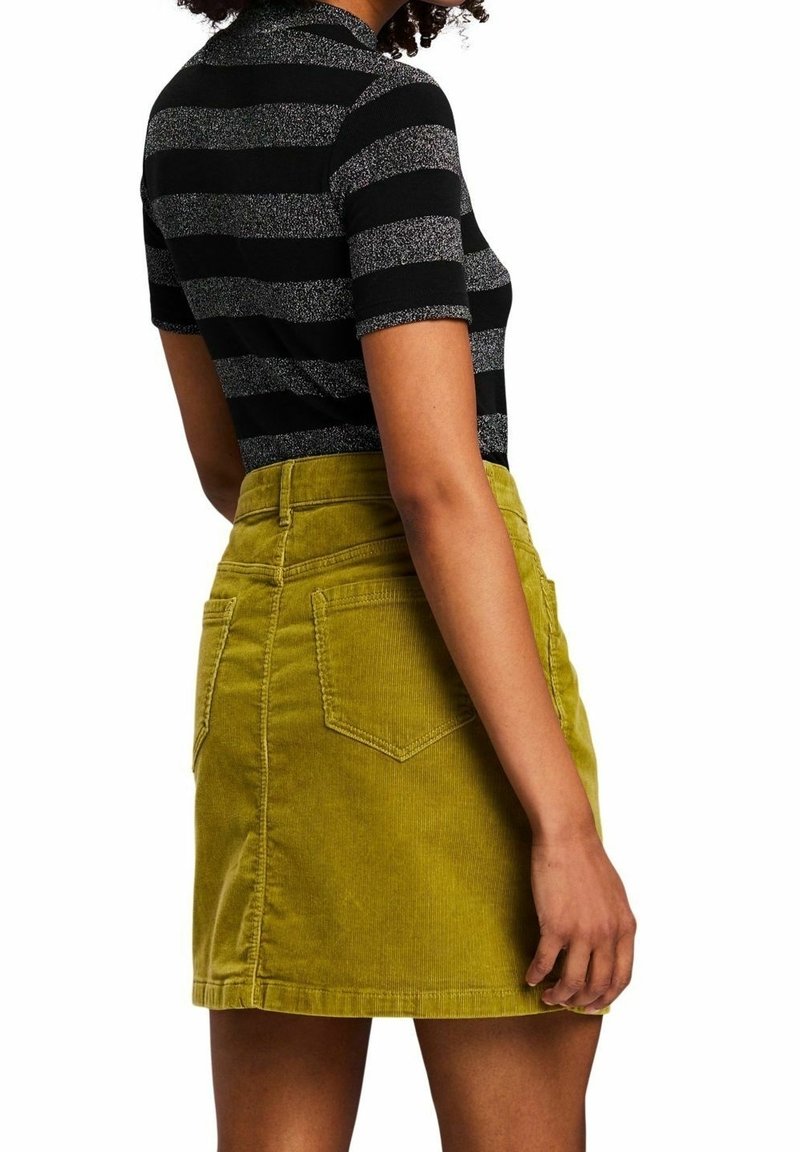Czarna i srebrna koszulka w paski z krótkim rękawem, zestawiona z zieloną mini spódniczką z sztruksu, posiadającą tylne kieszenie i teksturowane wykończenie.