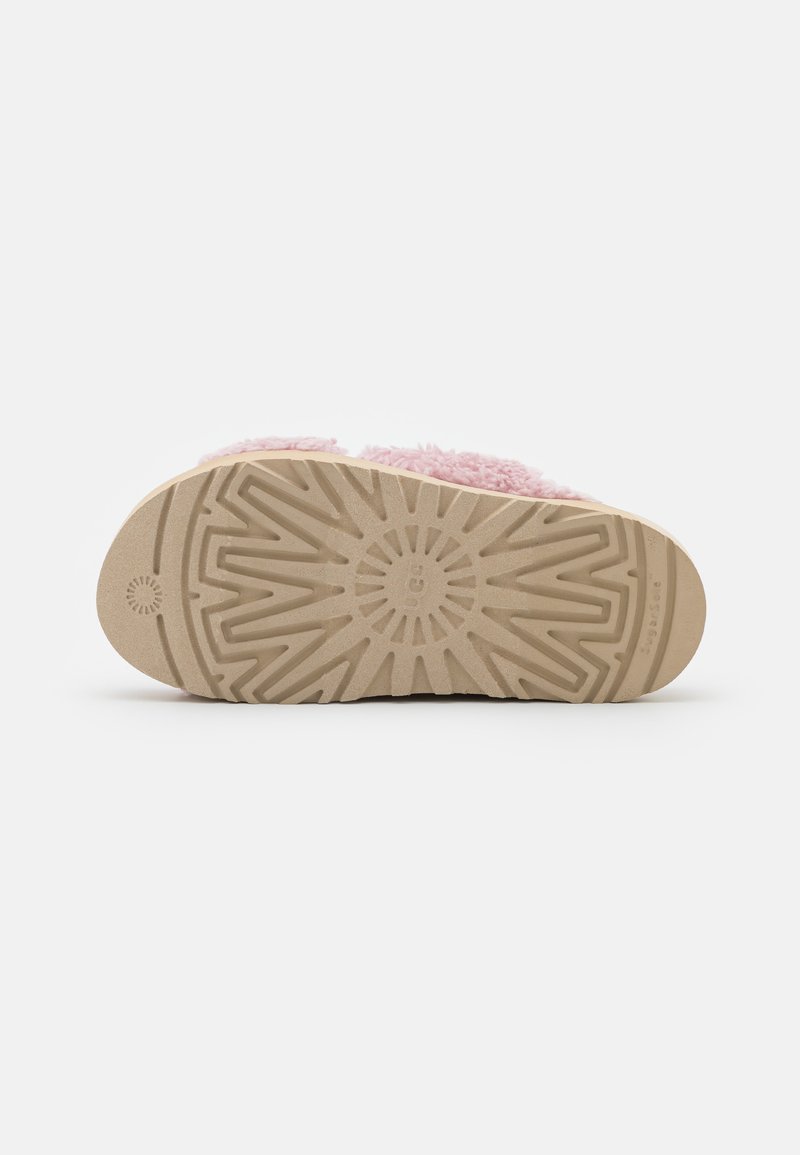 Suola marrone chiaro di una ciabatta con motivo a zigzag e radiale texturizzato, che mostra parzialmente la parte superiore rosa pelosa su uno sfondo bianco.