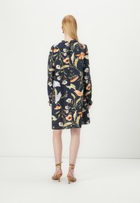 Vestido floral em tecido azul marinho escuro com flores vibrantes em laranja e branco, mangas longas e um corte descontraído. Combinado com sandálias de tiras bege.