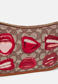 Brązowa torebka z wzorem, z sześcioma łatami w kształcie czerwonych ust, ozdobiona cekinami i haftem, z złotym zamkiem błyskawicznym na górze.